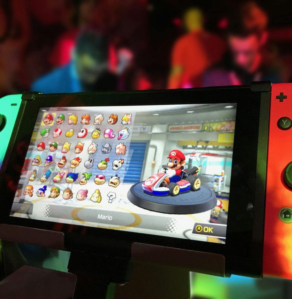 pexels-photo-371924-371924 Close-up of a Nintendo Switch showing Mario Kart selection screen, gaming atmosphere in the background.